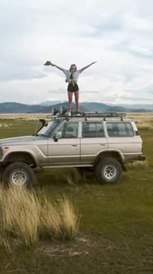Woman Celebrates Adventure on Car Roof in Nature