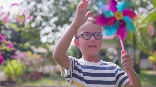 Boy in glasses is playing with pinwheel in a garden