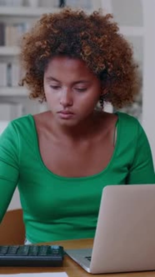 Young Woman Studies at Home While Using Laptop and Calculator for Work