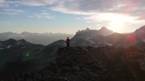 Adventurous Person Stands Victorious on Mountain Peak Watching Breathtaking Sunset