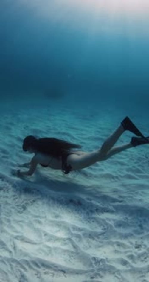 Woman Glides Underwater Over Sandy Sea Bottom in Blue Ocean with Sunshine Freediving with Sexy Woman