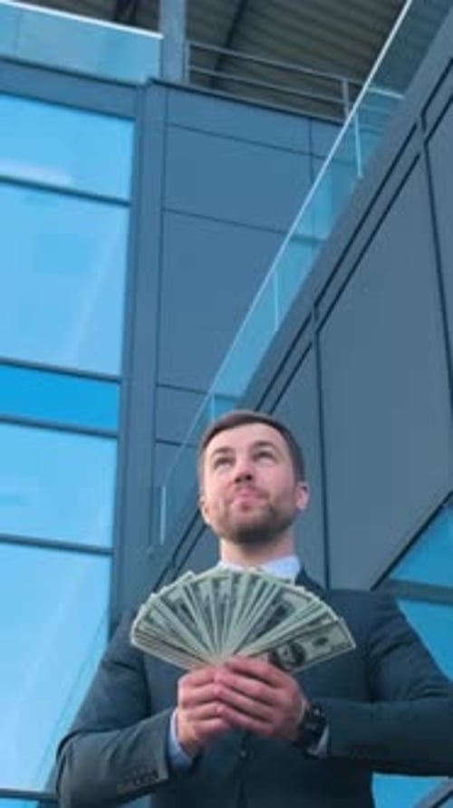 Man in Electric Blue Suit Smiles Holding Fan of Money in Front of Building