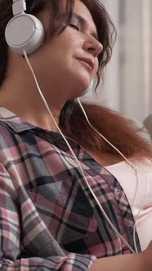Woman Listens to Music with White Headphones Indoors