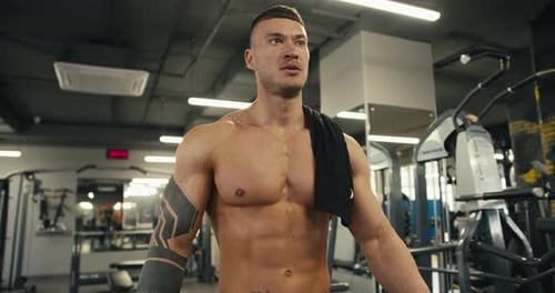 A Young Male Athlete with a Naked Torso and a Tattoo Walks Through the Gym