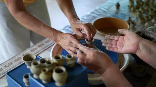 Gros plan des mains de deux femmes en train de poter l'une en apprenant l'autre sur un tour de potier modelant un