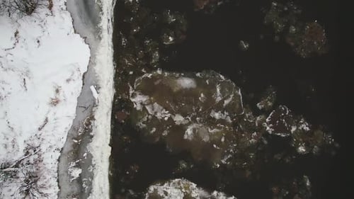 Aerial View of Frozen River Rocks Surrounded By Icy Waters and Snowcovered Banks