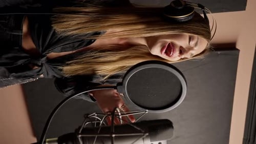 girl singer singing in a recording studio with headphones in front of microphone to create a song