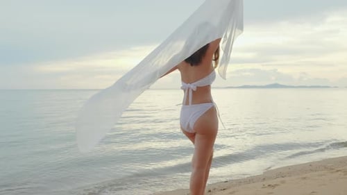 woman wear bikini swimsuit with blowing sarong enjoying walking and spin body at beach