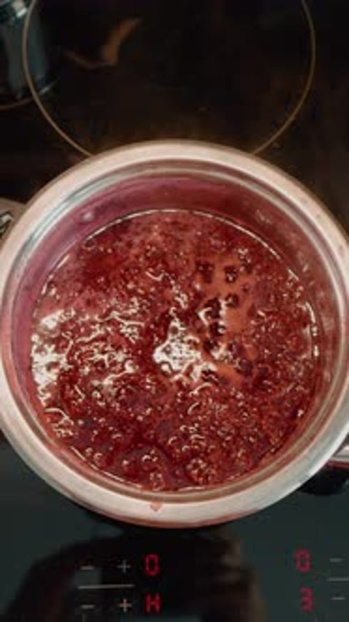 Vertical video Homemade raspberry jam cooking process in a modern kitchen