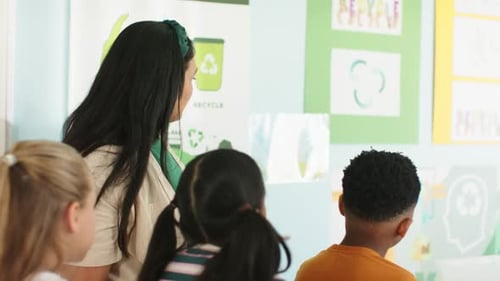 African American teacher with kids noticing chart, pointing to recycling and teaching at school