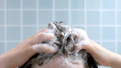 Female hands wash their hair with shampoo with foam on blue background, front view.