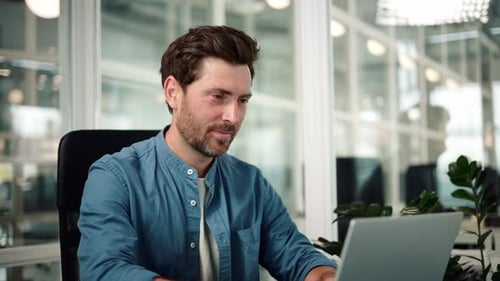 Serious Businessman Sitting at Remote Workplace with Laptop Thinking in Office