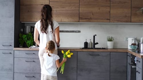 Child Gives Flowers to Smiling Mother in Kitchen