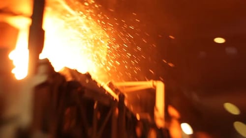 Intense close-up of sparks flying from molten metal in a foundry, glowing warmly