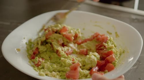 Preparing fresh guacamole dip with avocado and tomato