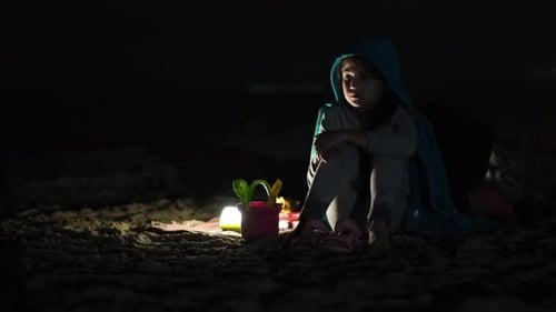 Child Sitting Alone on Sandy Beach Against Black Background on Summer Night