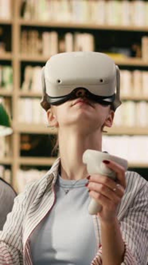 Vertical Video Student Wears VR Glasses and Holds Controllers in University Library