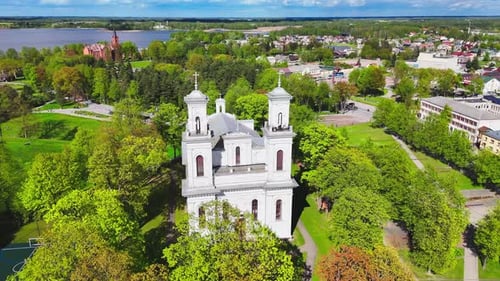 Twin-tower white church among spring trees in scenic riverside town – aerial view