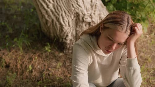 Pensive Woman Sitting by Tree in Park
