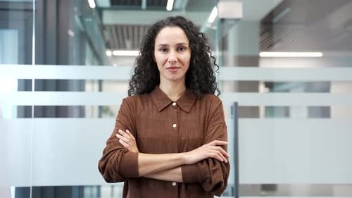 Portrait of smiling businesswoman standing with crossed arms at workplace in modern business office.