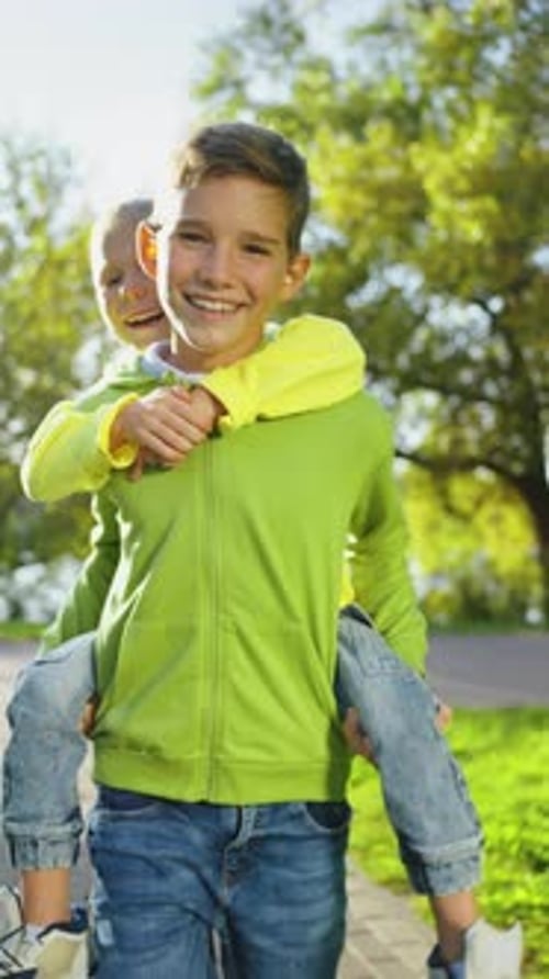 Vertical: niño feliz montado en la espalda de su hermano en el parque, sonriendo a la cámara