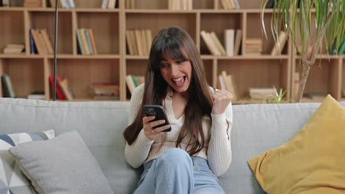 Excited Woman Celebrating Success on Cell Phone Indoors