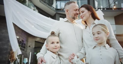 Happy Family in Similar Outfits Smiling and Cuddling in Restaurant Terrace