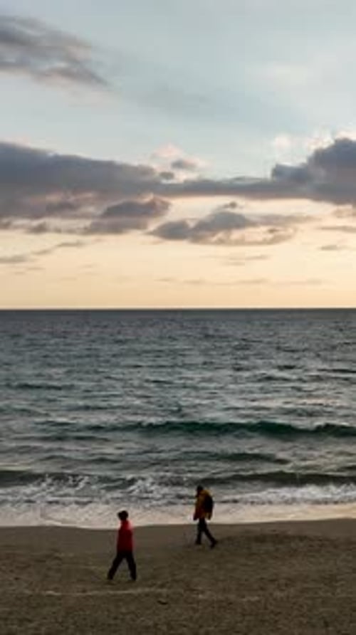 Vertikales Video: Ruhiger Spaziergang bei Sonnenuntergang Luftaufnahme eines magischen Strandes mit Spaziergängern