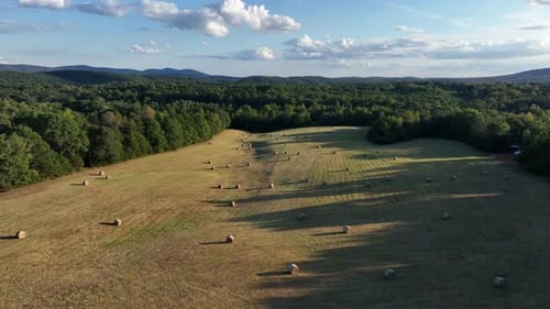 Several hay bales of agricultural farm fields surrounded by forest trees and mountains. Sunny