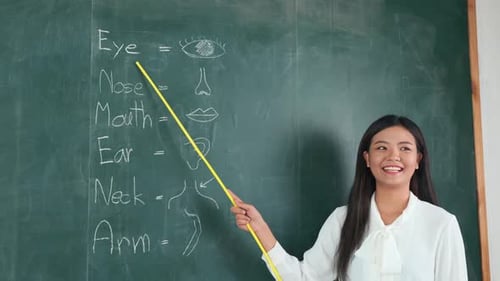 Young Woman Teaches at Chalkboard in Classroom