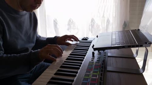 Man Playing MIDI Keyboard with Laptop in Home Studio Setup.