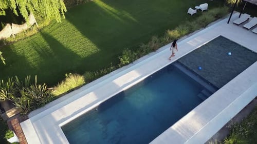 High angle camera follows woman walking beside pool in beautiful yard