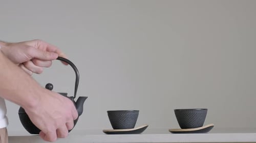 Male Hands Pour Tea Into Cup From Black Teapot. Tea Set. wide