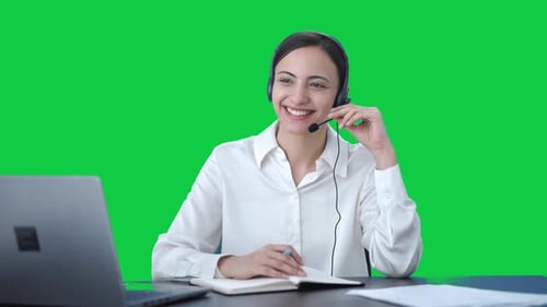 Happy Indian call center girl talking to customer and taking notes Green screen