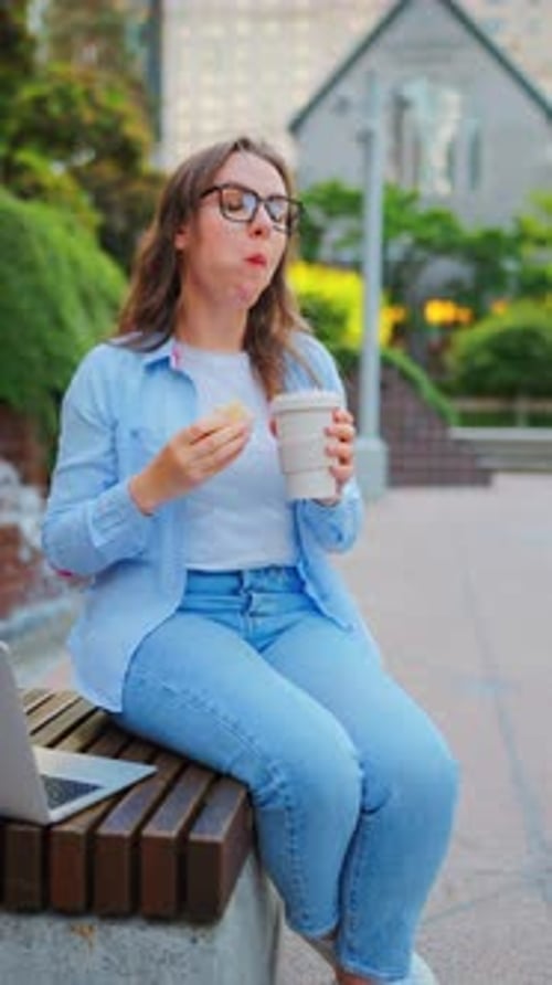 Frau beim Mittagessen mit einem Sandwich und Kaffee im Park mit einem Laptop