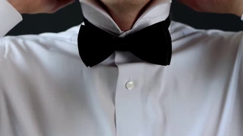 Ein Mann, der eine schwarze Fliege auf einem weißen Hemd anpasst, Vorbereitung für eine formelle Veranstaltung oder Hochzeit