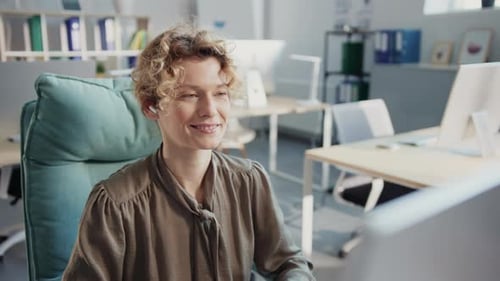 A Professional Woman Works at a Desk Using a Desktop and Laptop