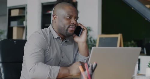 Successful African American Manager Consulting Client on Mobile Phone and Using Laptop in Office