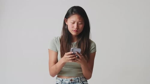 Young woman texting on her phone, isolated over white background in studio