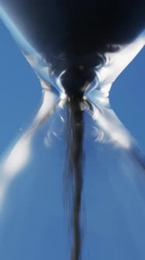 Vertical video of close up of hourglass with black sand pouring with copy space on blue background