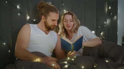 Smiling Couple Reading Book in Bed at Night