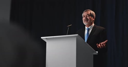 Adult Man Speaks at Podium in a Suit