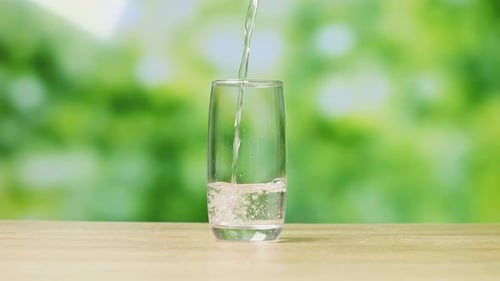 Trinkwasser wird auf einem Bur-Nature-Bildschirmhintergrund im Studio in ein Glas gegossen