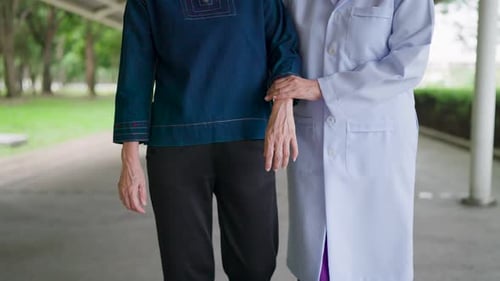 Close-up Asian nurse's hand supporting an elderly woman walking outside her home.