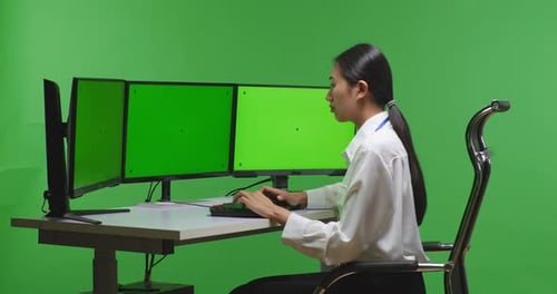Side View Of Asian Woman Working With Mock Up Multiple Computer Monitor In Green Screen Studio