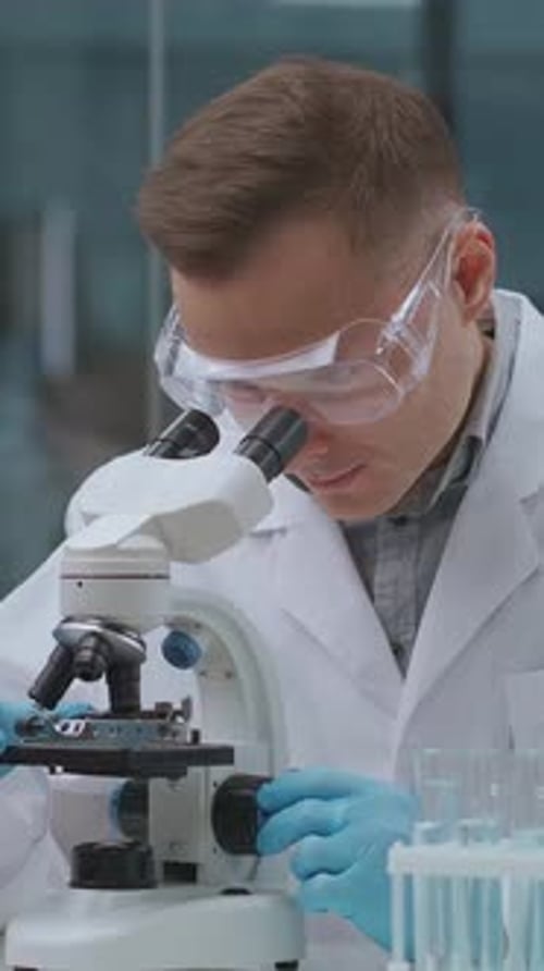 Scientist in Laboratory Using a Microscope for Detailed Analysis While Wearing Protective Goggles