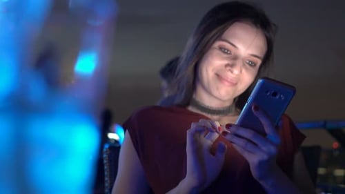 Young woman enjoys city nightlife browsing her smartphone on a rooftop terrace