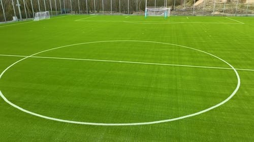 A well-maintained soccer field with bright green artificial turf and white lines marking the field.