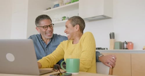 Happy Couple Laughing Together Using Laptop in Kitchen