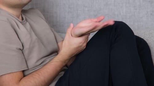 Man Rubbing Sore Wrist on Couch Indoors